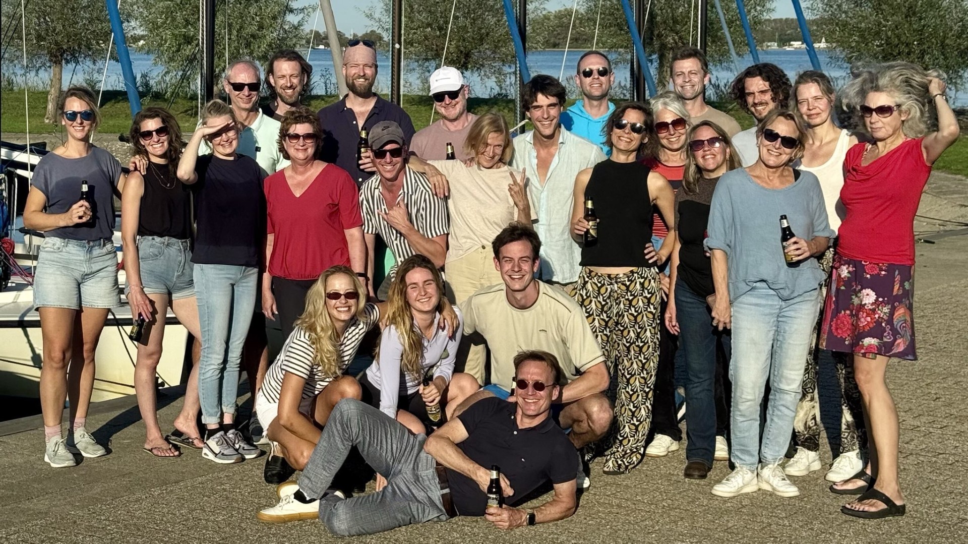 Een vrolijke groepsfoto van de collega's van de Argumentenfabriek bij een zeilschool tijdens een uitje in Zeeland in de zon.